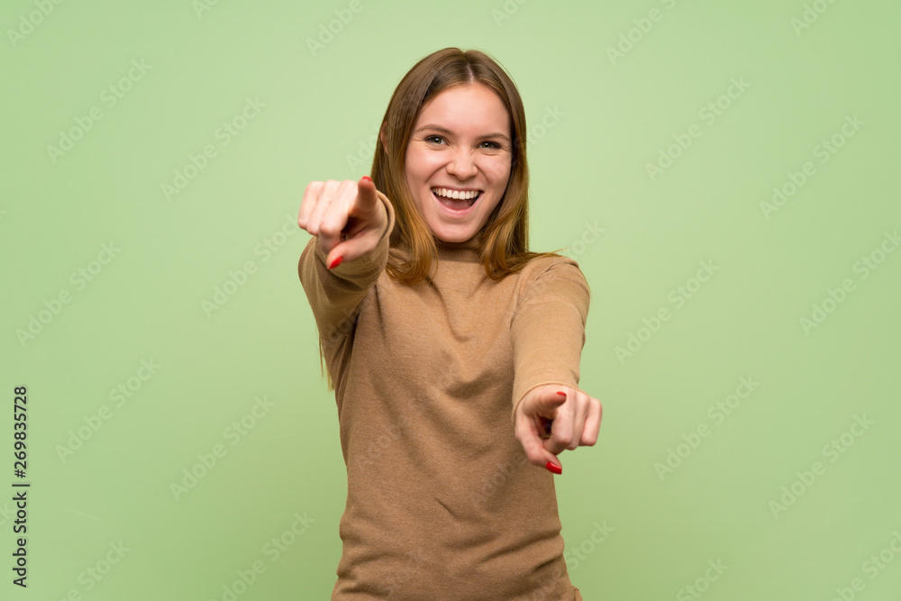 Young woman with turtleneck sweater points finger at you while smiling Young woman with turtleneck sweater points finger at you while smiling