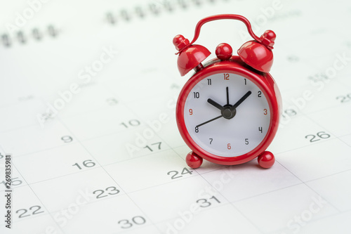 Date and time reminder or deadline concept, small red alarm clock on white clean calendar with number of day, counting down to holiday, vacation or end of month photo