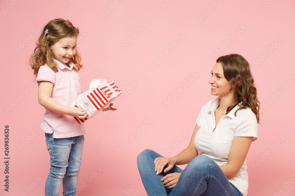 Woman have fun with cute child baby girl, hold present box. Mother, little kid daughter isolated on pastel pink wall background, studio portrait. Mother's Day, love family parenthood childhood concept Woman have fun with cute child baby girl, hold present box. Mother, little kid daughter isolated on pastel pink wall background, studio portrait. Mother's Day, love family parenthood childhood concept
