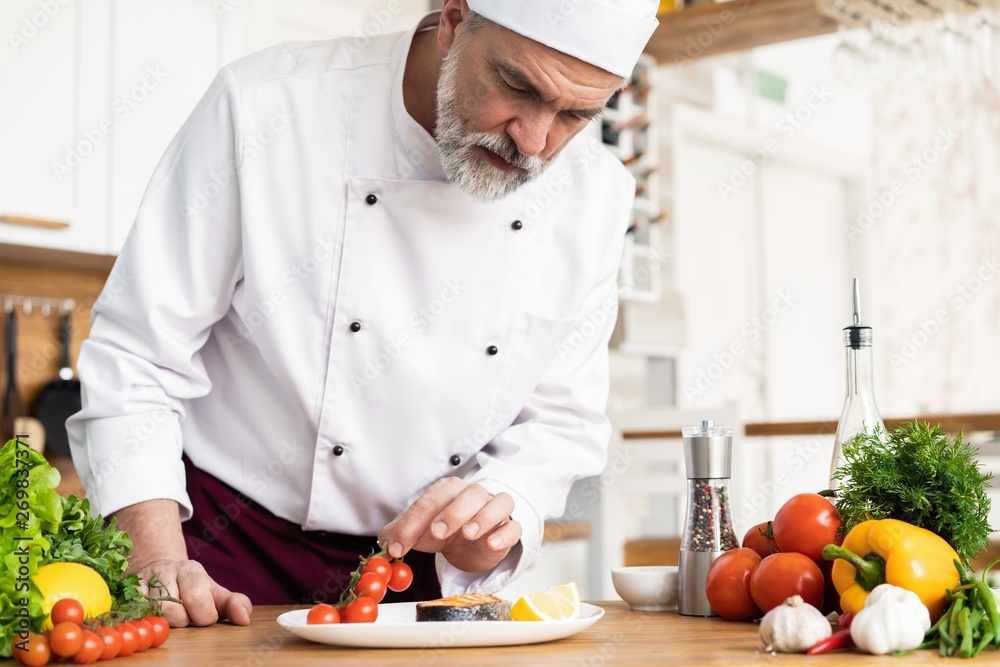Chef with diligence finishing dish on plate, fish with vegetables Chef with diligence finishing dish on plate, fish with vegetables