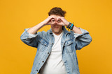 Portrait of young man in denim casual clothes hold hands near eyes imitating glasses or binoculars isolated on yellow orange background. People sincere emotions lifestyle concept. Mock up copy space.