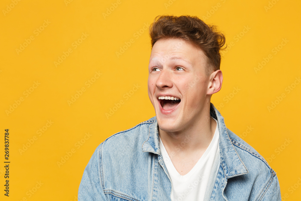 Obraz premium Portrait of laughing funny young man wearing denim casual clothes looking aside isolated on yellow orange wall background in studio. People sincere emotions, lifestyle concept. Mock up copy space.