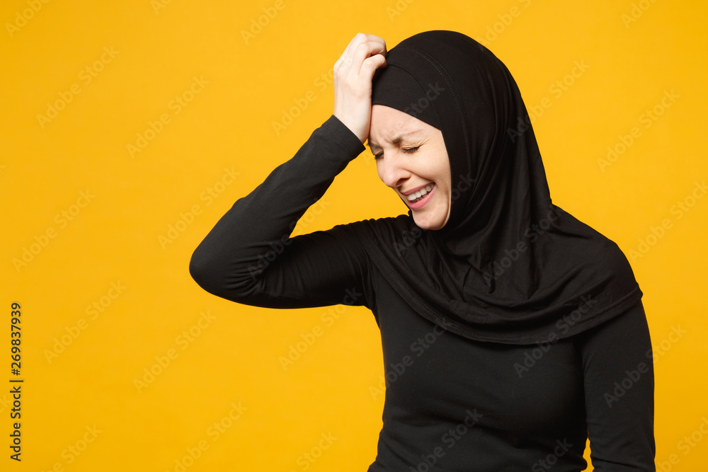 Sad upset crying confused young arabian muslim woman in hijab black clothes posing isolated on yellow wall background, studio portrait. People religious Islam lifestyle concept. Mock up copy space. Sad upset crying confused young arabian muslim woman in hijab black clothes posing isolated on yellow wall background, studio portrait. People religious Islam lifestyle concept. Mock up copy space.