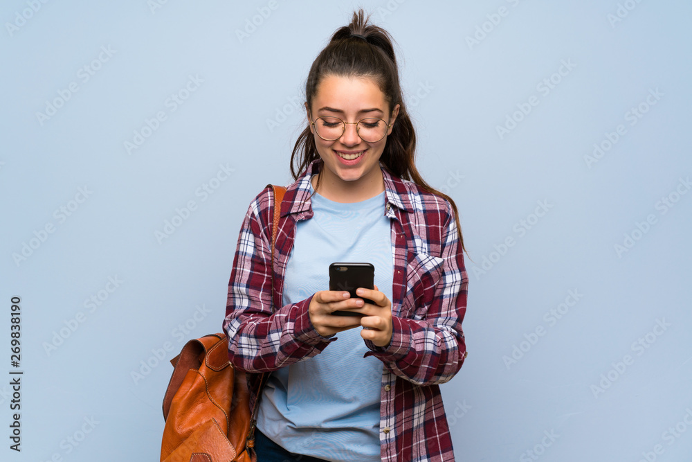 Teenager student girl over isolated blue wall sending a message with the mobile Teenager student girl over isolated blue wall sending a message with the mobile