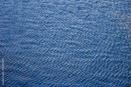 Blue lake water with ripples surface. Rippled water texture. Small waves in the pond. Fresh clean water texture. Selective focus. Copy space.