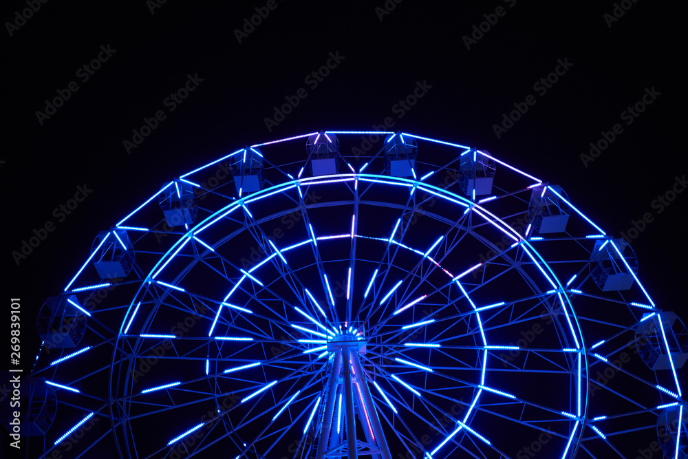 Glowing ferris wheel in an amusement park against a black night sky. Close-up