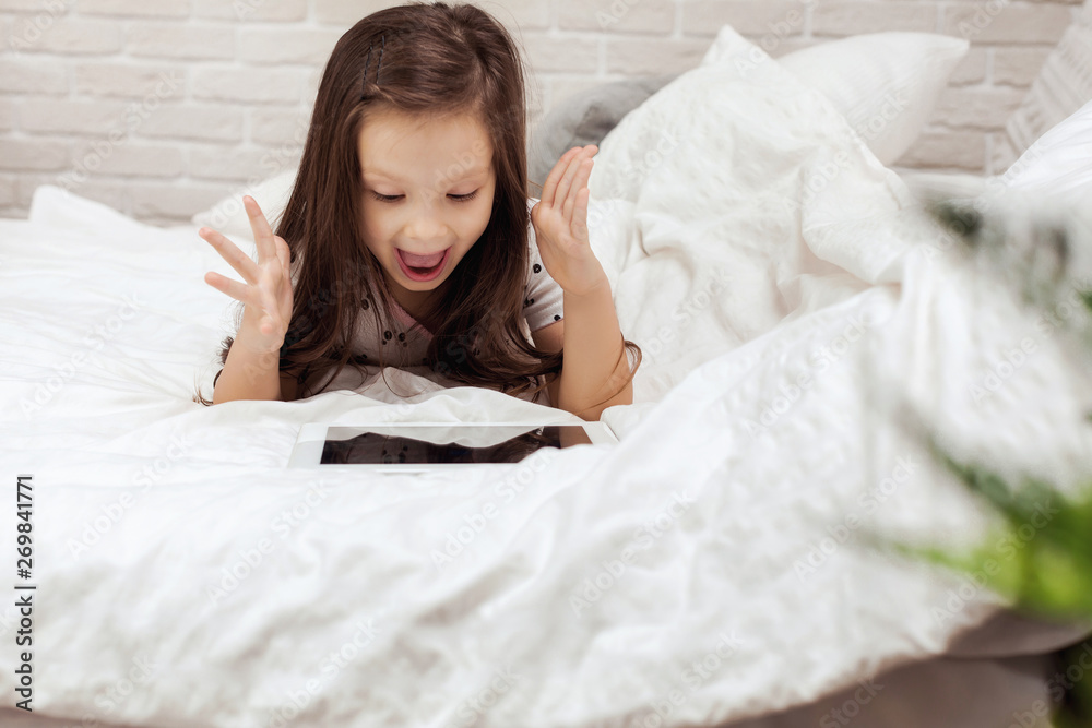 cute little child girl lies in bed uses digital tablet. child playing on tablet pc. cute little child girl lies in bed uses digital tablet. child playing on tablet pc.