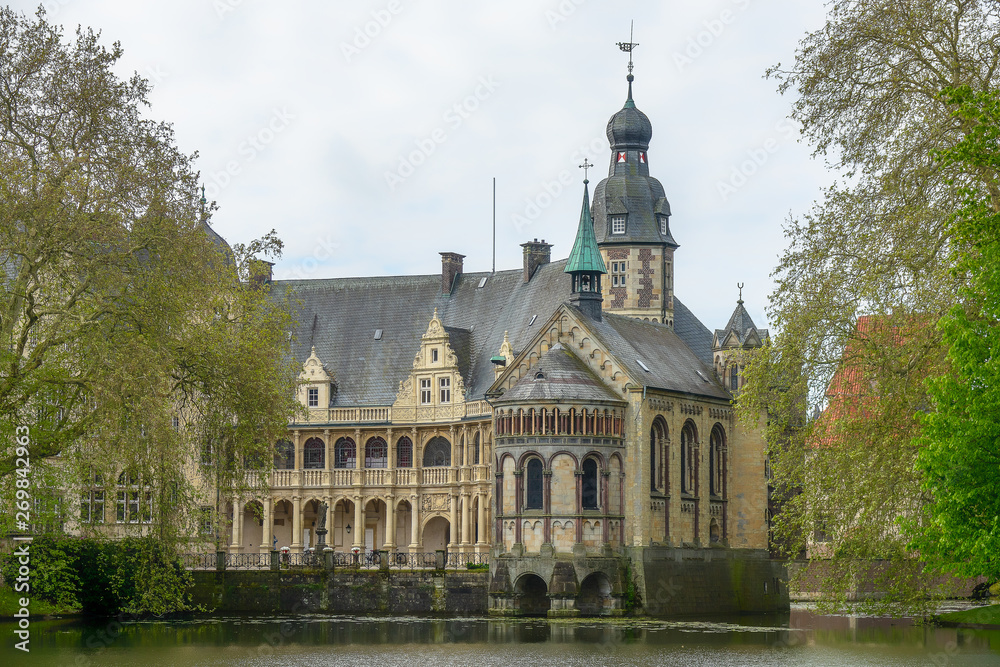 Fototapeta premium An old castle hundreds of years old by a lake. The building reflects in the water and is surrounded by trees.