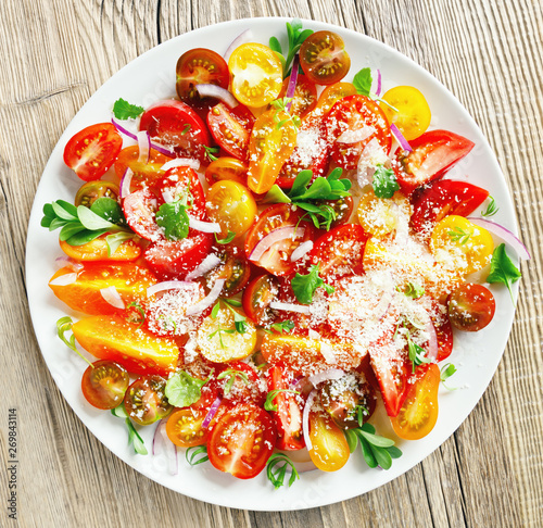 mix tomato variety salad with leaf vegetables and red onion seasoned with cheese, olive oil, and white wine vinegar