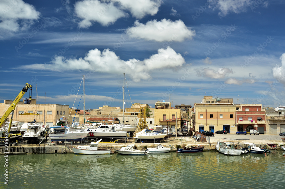 Kleiner Hafen mit Booten und Häusern auf Sizilien vor blauem Himmel mit Wolken