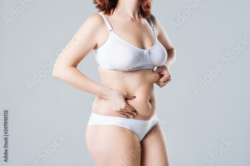 Woman with fat flabby belly, overweight female body on gray background