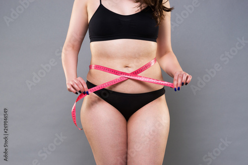 Woman with fat belly, overweight female body on gray background