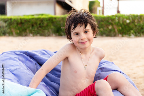 Portrait of a boy of seven years old sitting on a bean bag chair on the beach of the resort in summer. Religious child wearing christian cricifix on the neck photo