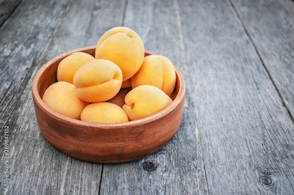 Ripe Golden apricots in wooden bowl on wooden background. Copy space