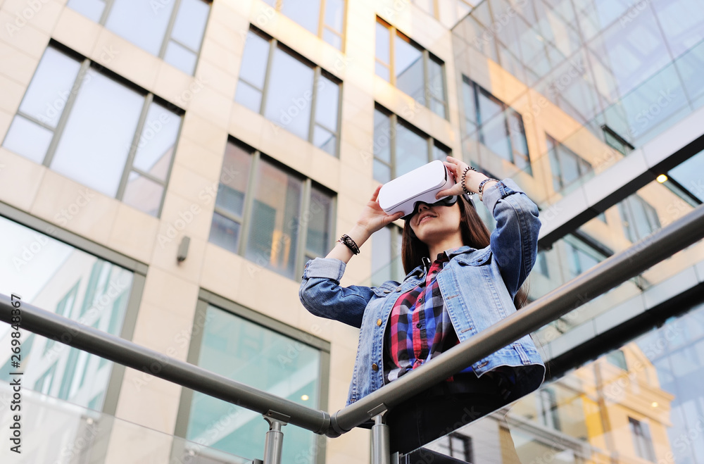 cute young woman with long hair in VR glasses on modern glass building background.