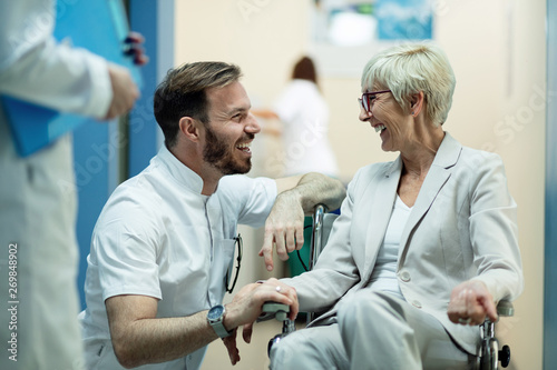 Happy senior woman in wheelchair talking to a doctor in a hospital.