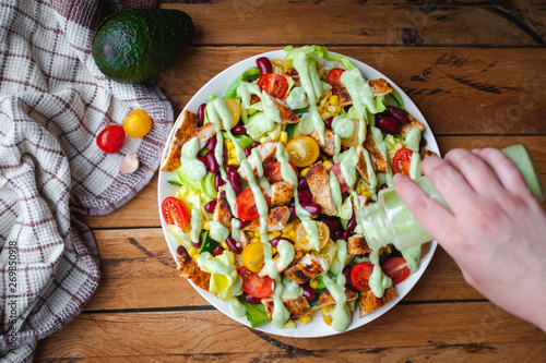 Close-up of chicken salad with fresh vegetables in a plate and avocado dressing, on wooden background, top view