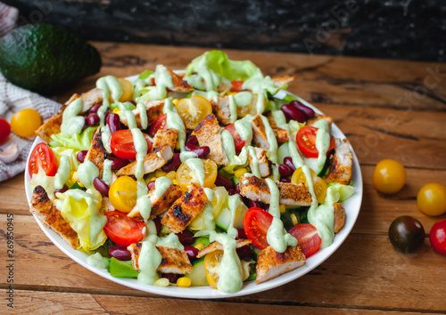 Close-up of chicken salad with fresh vegetables in a plate and avocado dressing, on wooden background