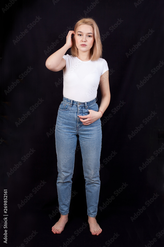 Young woman in white t-shirt and blue jeans is standing on a black background Young woman in white t-shirt and blue jeans is standing on a black background