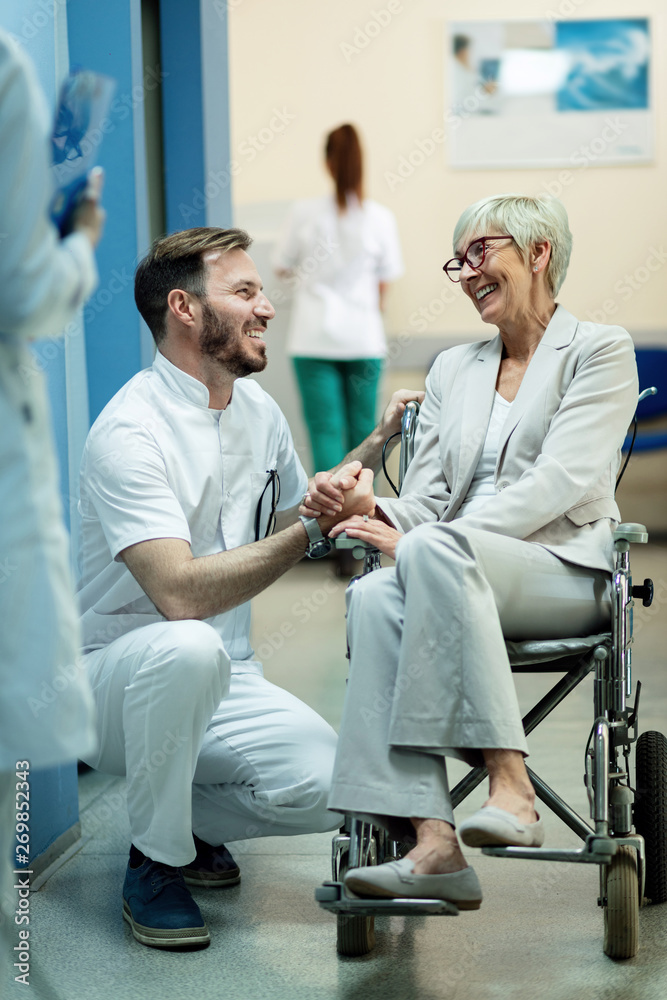 Obraz premium Happy doctor and disabled mature woman in wheelchair talking in the hospital lobby.