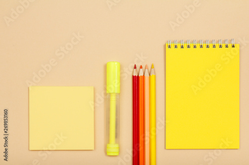 Note paper, felt pen, color pencils and notebook on beige background.