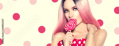Beauty sexy model woman with pink hairstyle and beautiful makeup holding lollipop candy over polka dots background