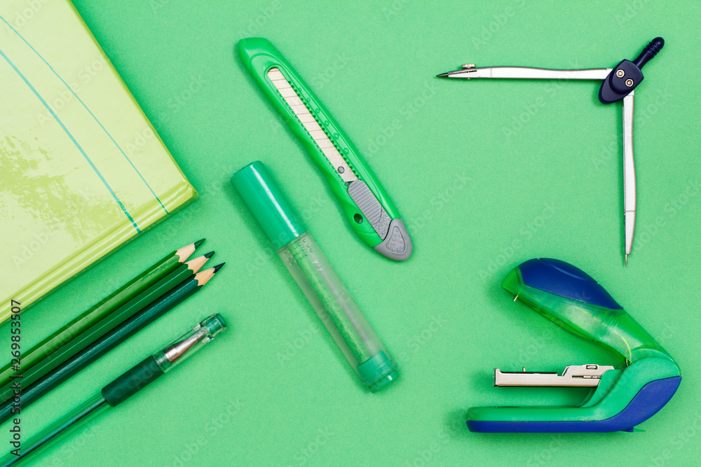 Book, color pencils, pen, felt-tip pen, paper knife, compass and stapler on green background. Book, color pencils, pen, felt-tip pen, paper knife, compass and stapler on green background.