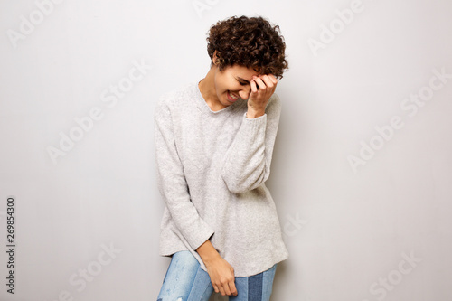 young woman laughing with hand to head by white wall