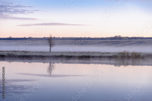 Dawn over the river on a summer morning, fog over the field, grass with hoarfrost