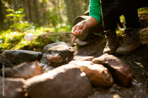 A girl sits by the fire in the woods drinking tea and roasting marshmallows