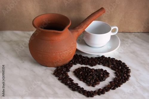 brown clay Turk for cooking coffee, white Cup and saucer and roasted coffee beans in the shape of a heart, selective focus