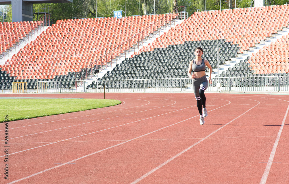 Fototapeta premium Beautiful athletic girl running around the stadium