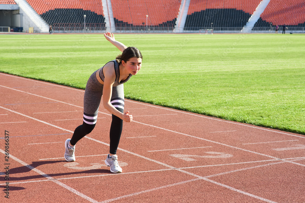 Fototapeta premium Young beautiful woman runner outdoor standing in start pose at the stadium
