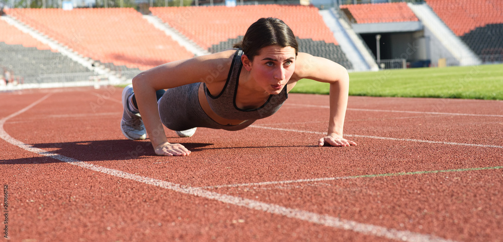 Obraz premium Beautiful and athletic girl push ups at the stadium