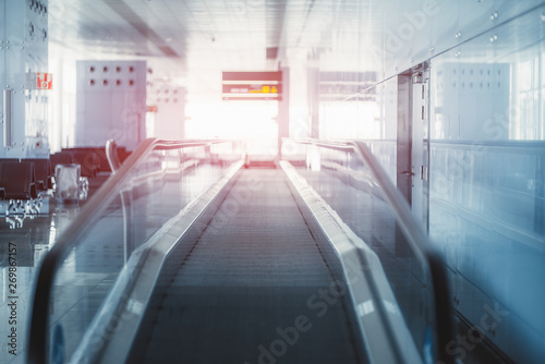 View of a modern travelator stretching into the vanishing point indoors of a railways station depot; moving walkway inside of a departure area of an airport terminal with a reddish flare at the end