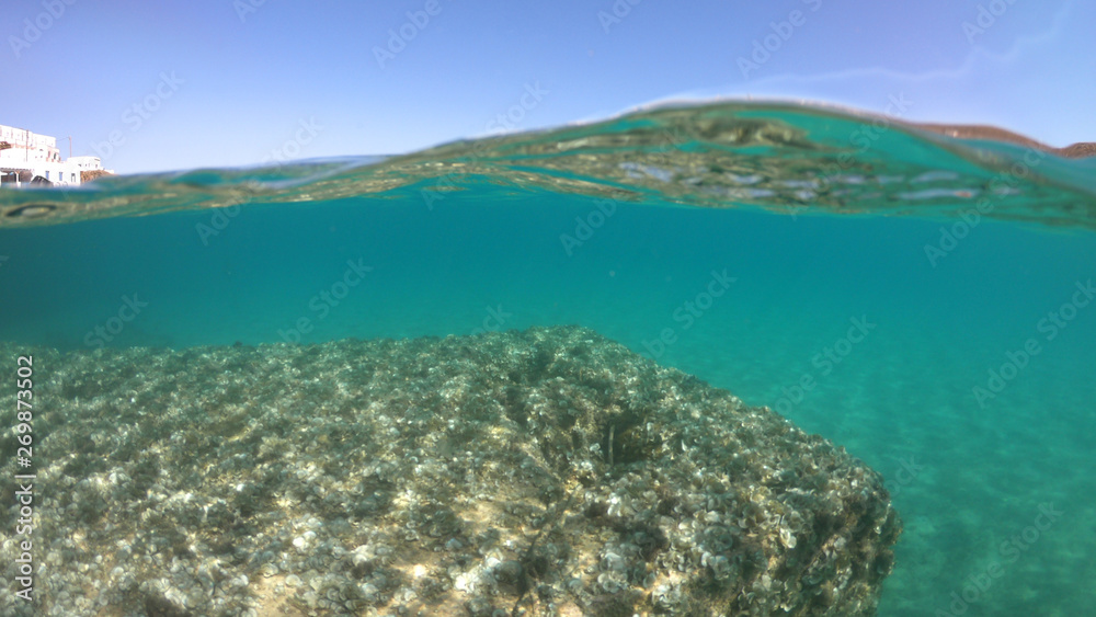 Underwater sea level photo of idilic pebble beach of Karavostasis, picturesque port of Folegandros island with traditional fishing boats docked and crystal clear turquoise sea, Cyclades, Greece