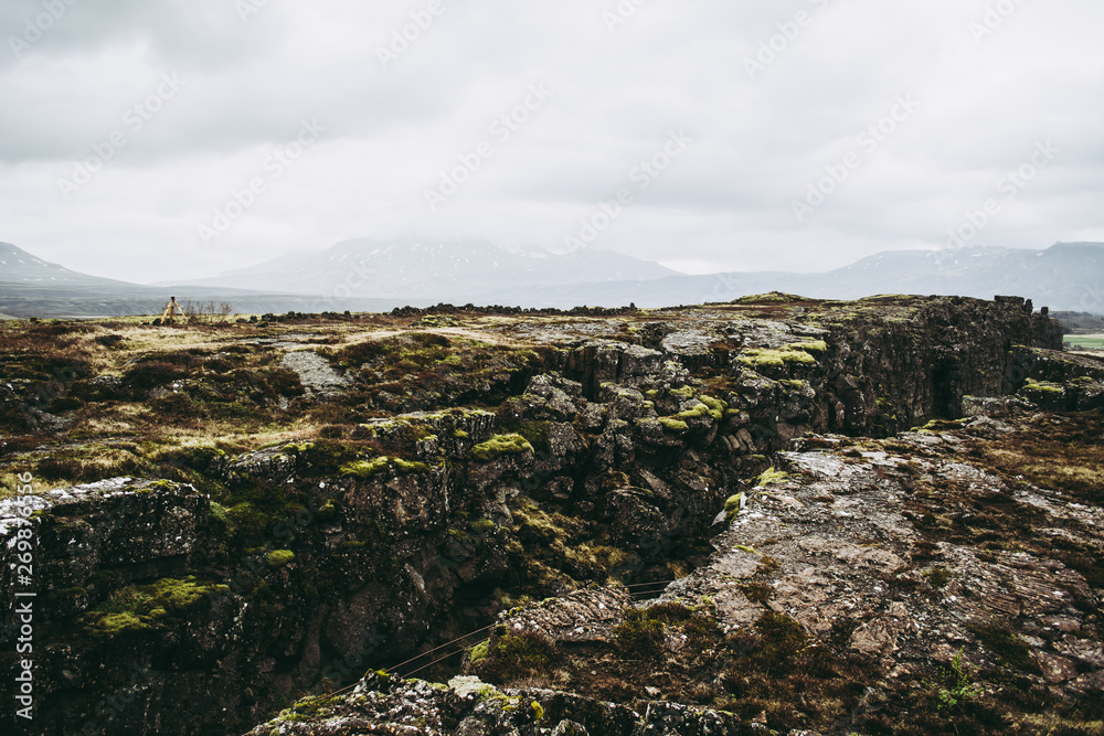 Cold bleak landscapes of Thingvellir National Park in Iceland in spring. Ancient rocks against dark misty mountains and gray sky
