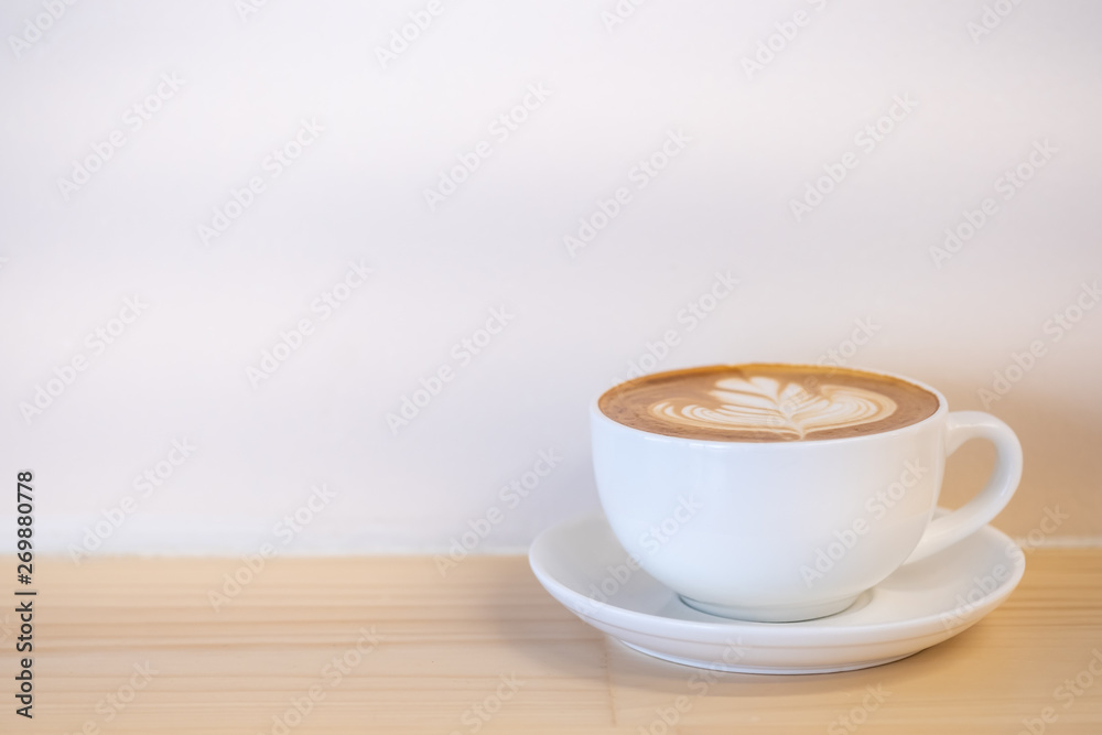 Obraz premium Close up of white cup of hot coffee latte with milk foam heart and flower shape art on wooden table with copy space for text.