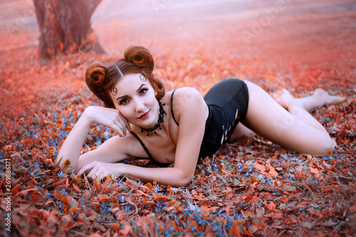 Tablou pe pânză A playful red-haired nymph is lying on a meadow with flowers like a kitty