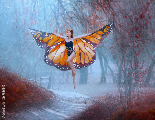 A bright, positive monarch butterfly enjoys flying. A young woman with a perfect body, long legs flies up into the sky. Huge, painted wings opened like a moth. Art processing. Cool blue background photo