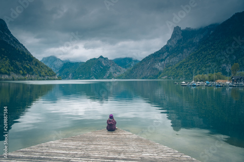 Kobieta samotnie siedzi na drewnianym pomoście nad górskim jeziorem Traunsee w Austrii w pochmurny dzień 