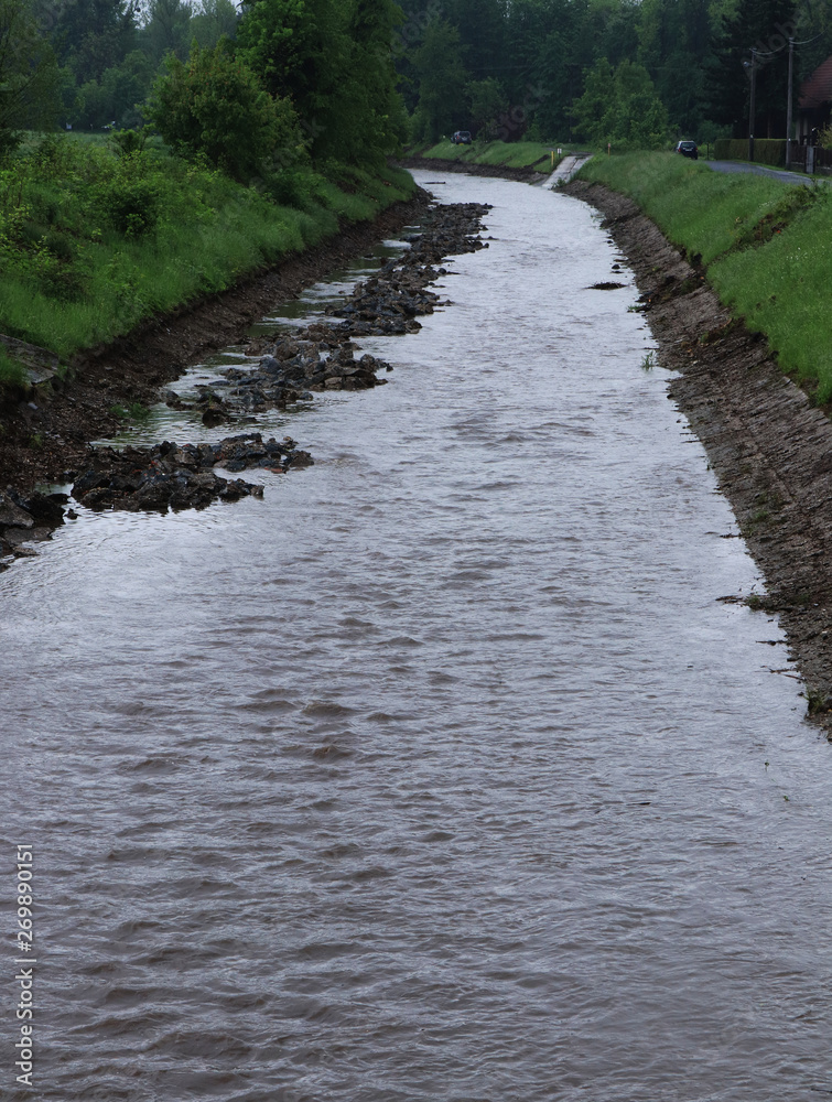 Water stream in river bed where water shouldn't be. Artificial created canal for transport some woods, small bags and so on. Floods in the Czech Republic, in may 2019 Water stream in river bed where water shouldn't be. Artificial created canal for transport some woods, small bags and so on. Floods in the Czech Republic, in may 2019