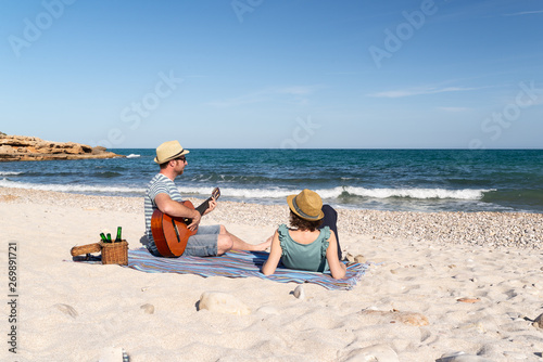Man woman couple playing the guitar and relaxing at a mediterranean beach in a sunny day