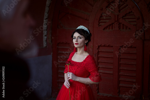 Sad princess with a rose  she is in a red dress and with a diadem on her head.