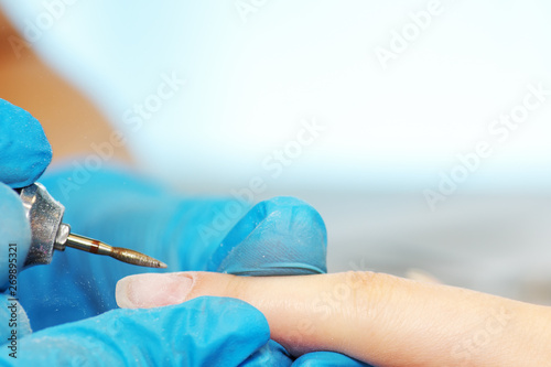 Closeup hardware manicure in a beauty salon. Manicurist use electric nail file drill to manicure on a female fingers.