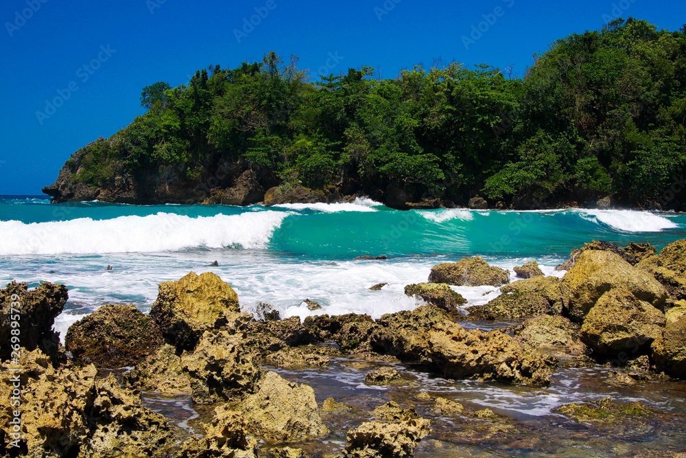 View beyond sharp rocks on turquoise rough sea with wave breakers and strong surf - Port Antonio, San San Beach, Jamaica