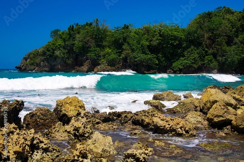Fototapeta Naklejka Na Ścianę i Meble -  View beyond sharp rocks on turquoise rough sea with wave breakers and strong surf - Port Antonio, San San Beach, Jamaica