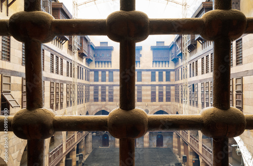 View of the courtyard of caravansary (Wikala) of al-Ghuri through window with iron ornate grid, showing vaulted arcades and interleaved wooden grids (mashrabiya), Cairo, Egypt photo