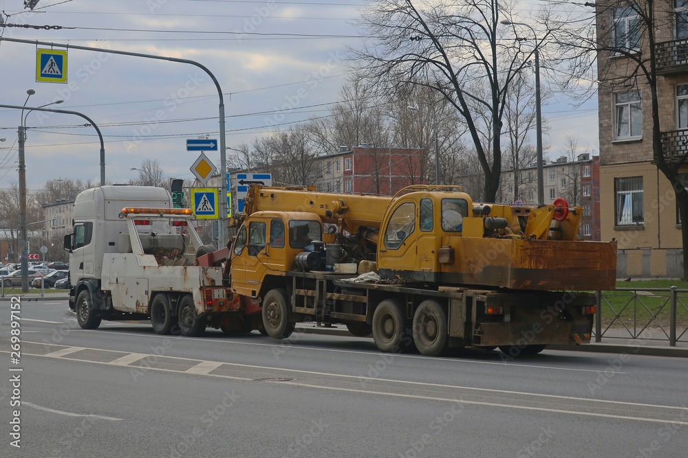 tow truck towing a broken truck crane down a city street