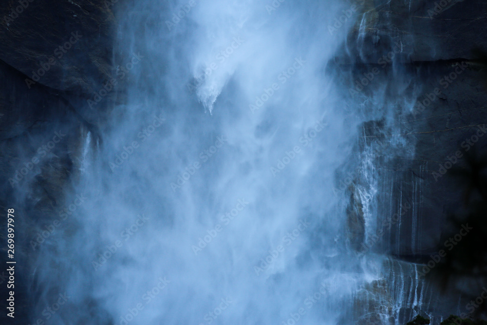 Misty blue waterfall in Yosemite with a cliff in the background
